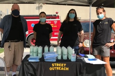 four surgical masked people stand behind an outdoor booth