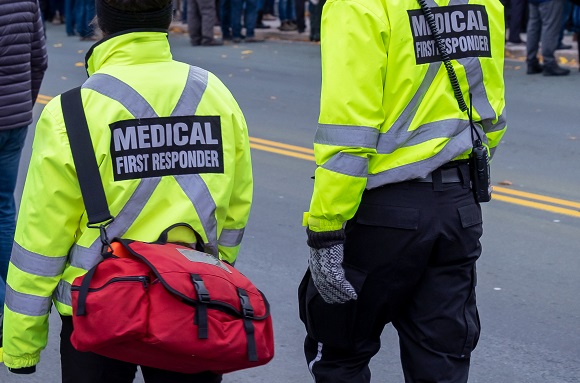 two medical first responders in neon yellow jackets walking down a crowded street