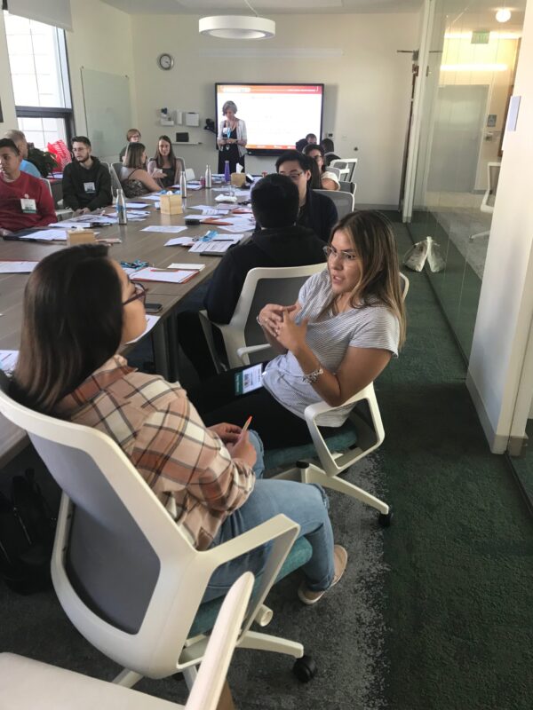 2 women talking in the foreground of a busy conference room