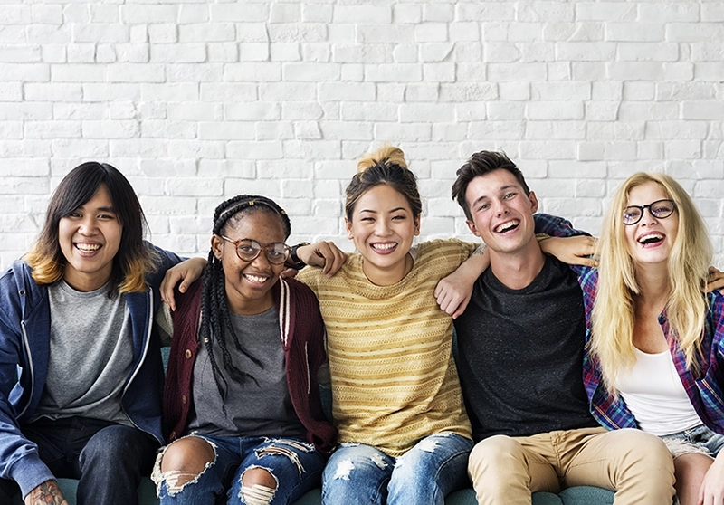 group of smiling young people sitting together on a couch