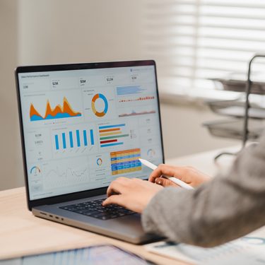 Businesswoman analyzing financial performance charts and dashboard data on laptop screen at office desk