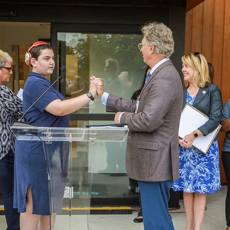 Patrick Maynard shakes hands with a client over a lectern