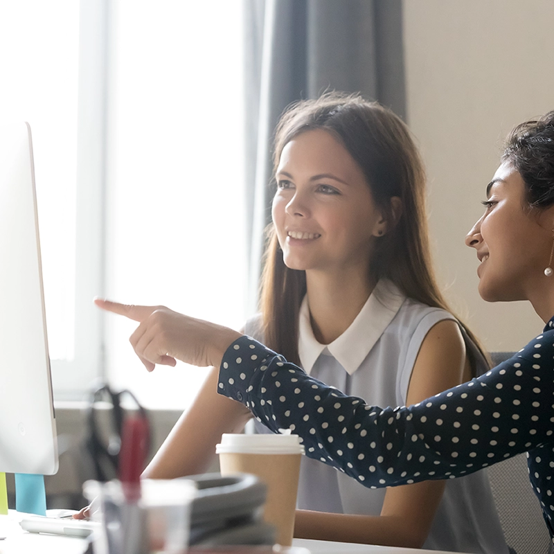 two women at a desk, one pointing out something on a monitor