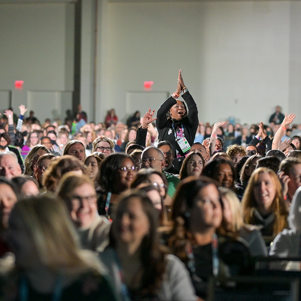 smiling woman stands up and claps in a large audience