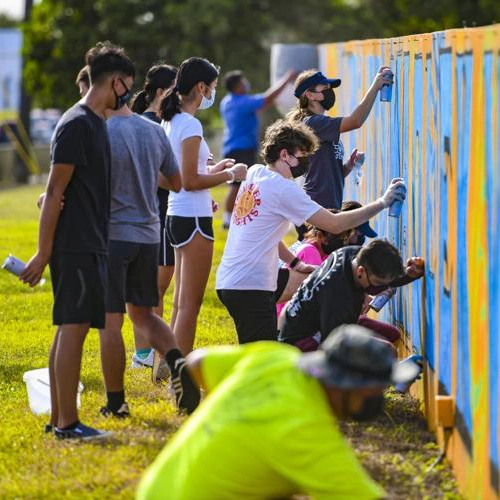 large group of people spray paints art on a wall