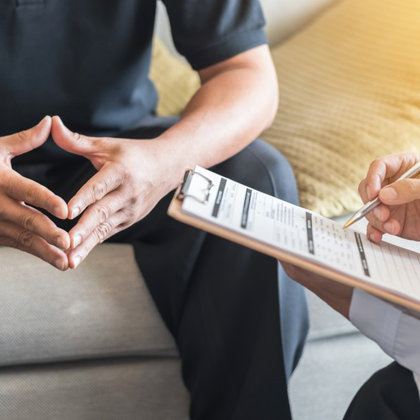 man sits with hands tented while doctor reviews a chart