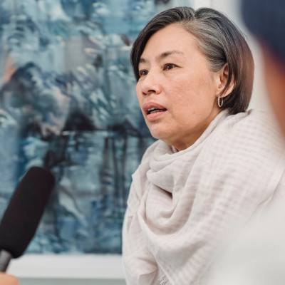 woman sits in front of a microphone, sharing her story