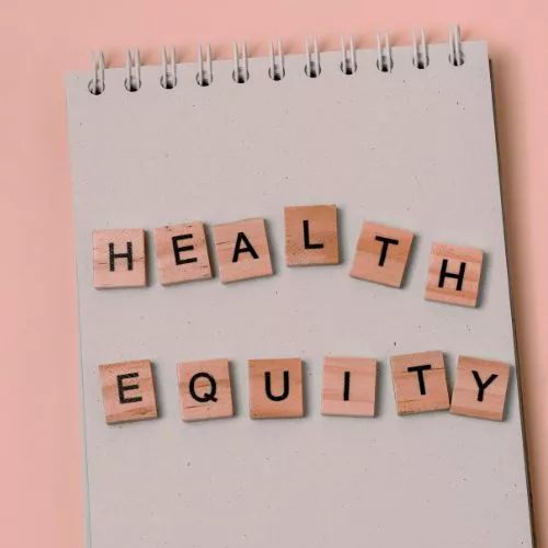 scrabble pieces spelling health equity sit atop a notebook