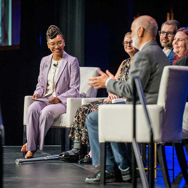 a panel of people sit on a stage and talk