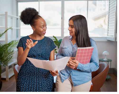 two people holding folders talk in an office