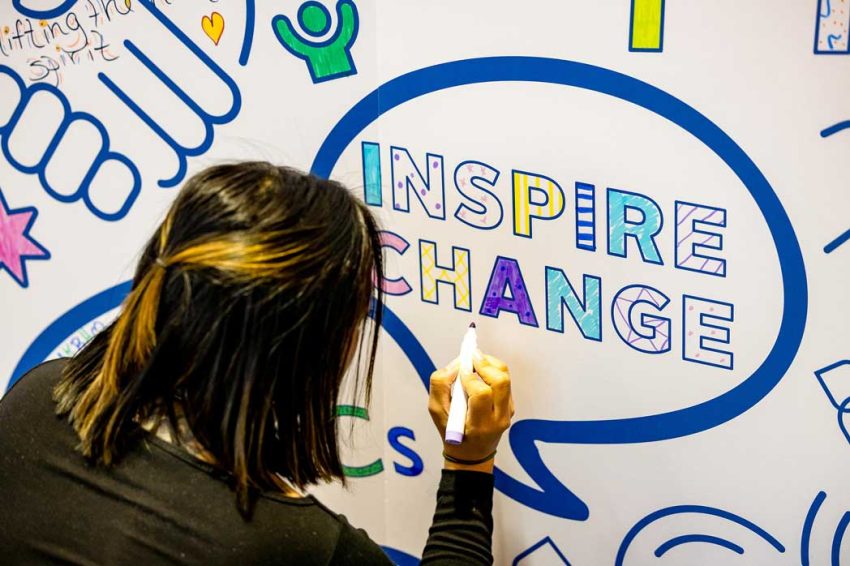a woman colors in the words Inspire Change on a wall