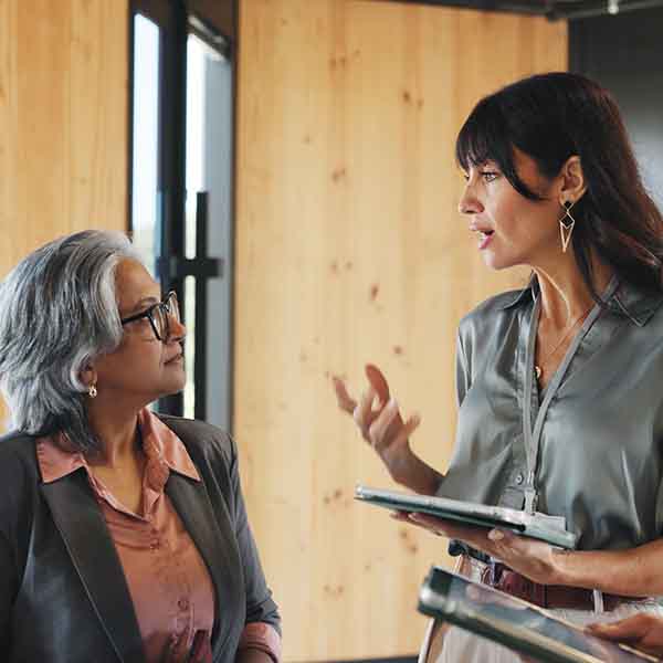 a woman with an ipad speaks to another woman in an office