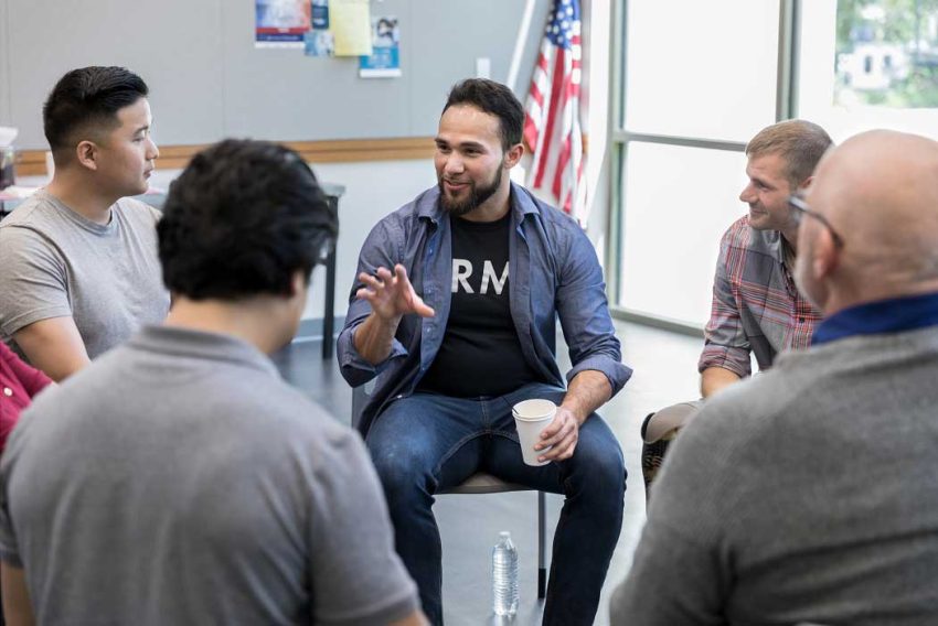 a man sits in a group in chairs and speaks